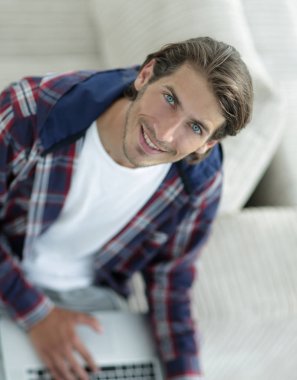 dizüstü bilgisayarda çalışan ve kameraya bakarak bir genç adam. Yukarıdan görüntülemek