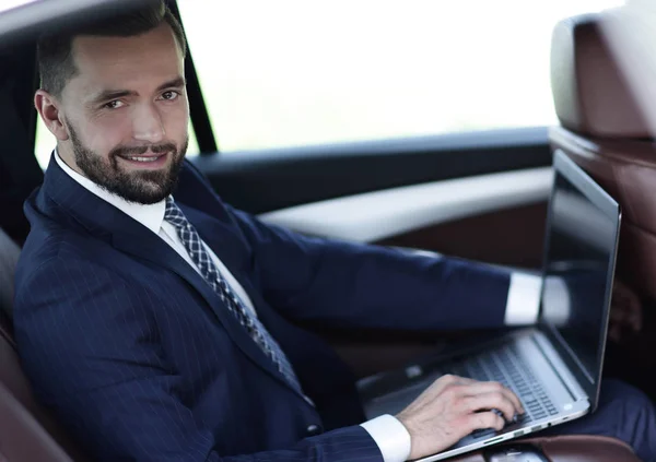 Uomo d'affari fiducioso con computer portatile seduto in auto . — Foto Stock