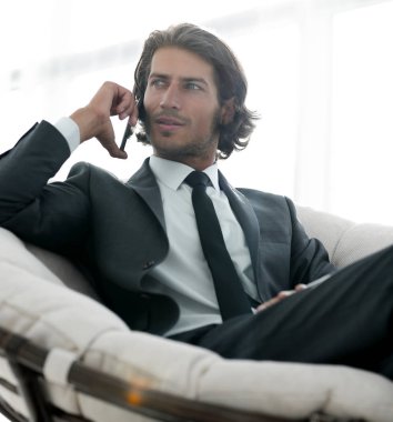 iş adamı rahat bir sandalyede otururken Smartphone'da konuşuyor.