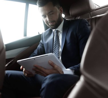 bir arabanın arka koltuğunda oturan bir dijital tablet ile işadamı