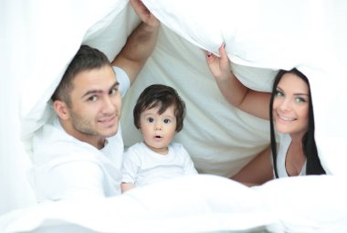 mutlu bir aile kameraya bakarken bir yorgan altında poz