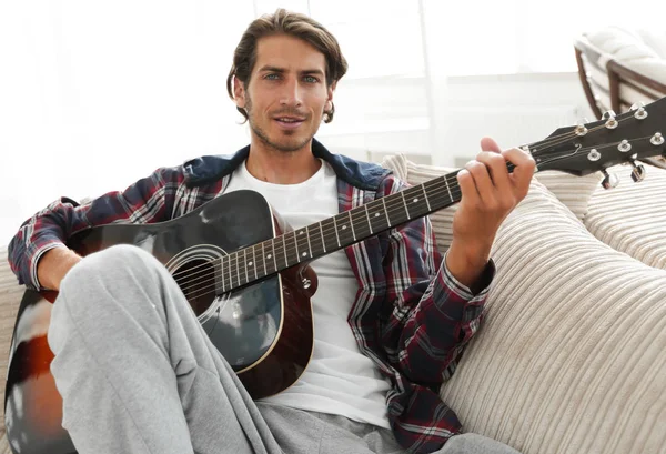 Cara moderno com guitarra sentado no sofá na sala de estar . — Fotografia de Stock