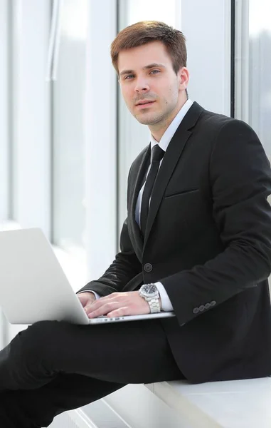 Молодой профессионал с ноутбуком на фоне офисного окна — стоковое фото