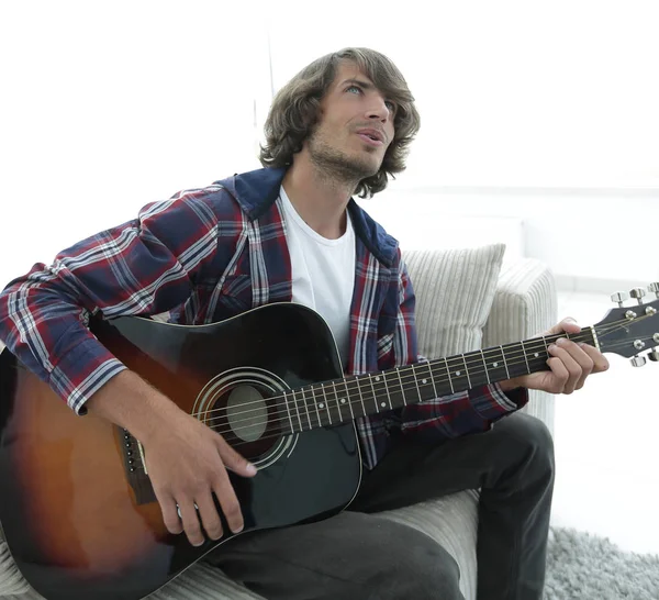 Um tipo moderno a tocar guitarra sentado no sofá. conceito de um estilo de vida — Fotografia de Stock