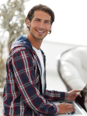 dizüstü bilgisayarda çalışan ve kameraya bakarak şık genç adam