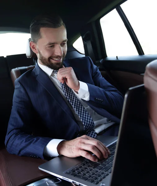 Hombre de negocios lee información sobre el ordenador portátil mientras está sentado en el coche —  Fotos de Stock