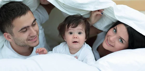 Família feliz posando sob um edredom enquanto olha para a câmera — Fotografia de Stock