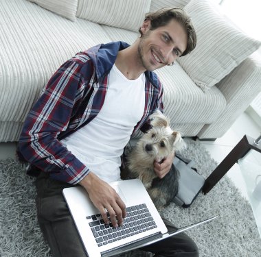 yakışıklı adam köpeğini sarılma ve kanepede oturan dizüstü bilgisayar ile