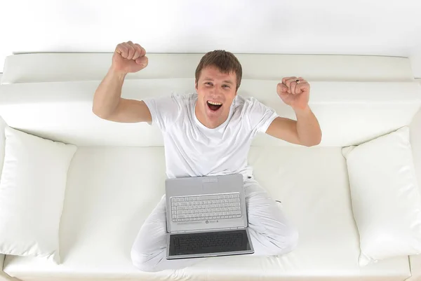 Happy young man sitting on the couch with arms up. — Stock Photo, Image