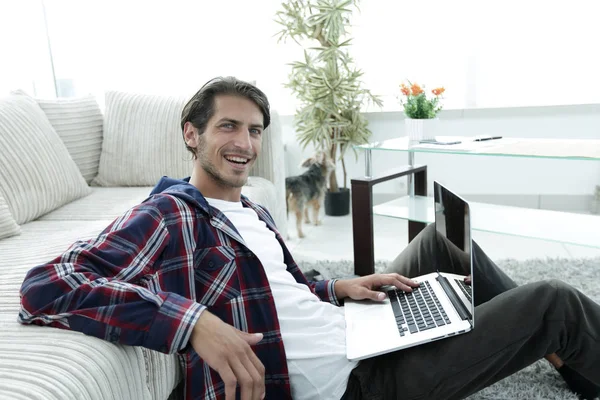 Encantador jovem com laptop sentado na sala de estar moderna — Fotografia de Stock