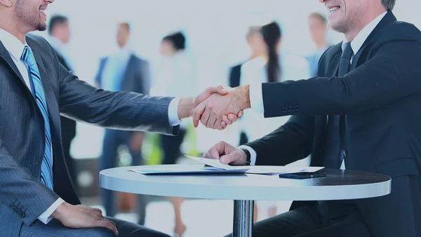 Collega's zitten aan een tafel tijdens een ontmoeting met twee mannelijke executives handen schudden — Stockfoto