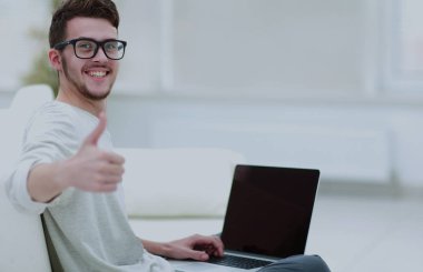 Diz üstü kullanarak ve başparmak gösterilen genç adam. Yakın çekim.