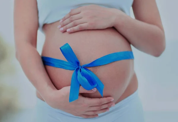 Woman holding hands on her baby bump, tied with a blue bow — Stock Photo, Image