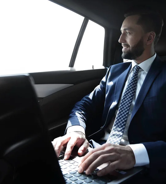 Χαμογελώντας επιχειρηματίας με laptop κάθεται σε αυτοκίνητο — Φωτογραφία Αρχείου