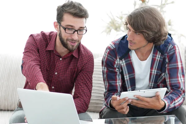 Dois jovens trabalhando com laptop e tablet sentado no sofá — Fotografia de Stock