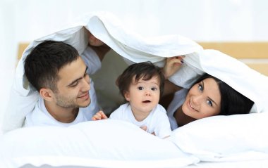 mutlu bir aile kameraya bakarken bir yorgan altında poz