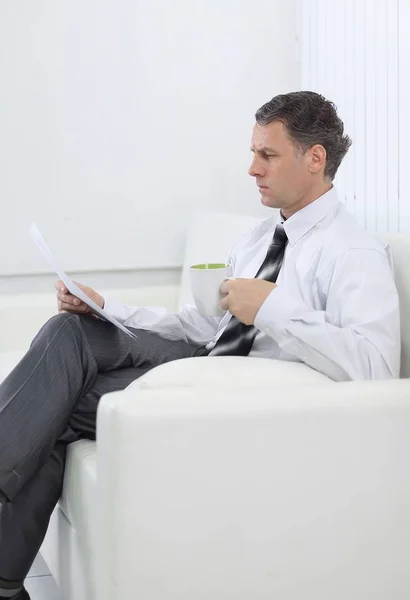 Businessman reading a document while sitting in a chair in the hotel room. — Stock Photo, Image