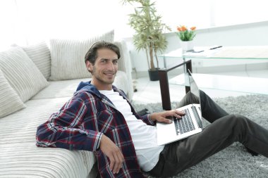 kanepede yakın katta oturan dizüstü bilgisayar ile gülümseyen genç adam