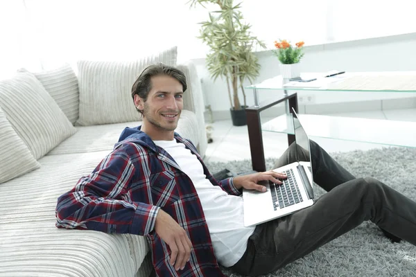 kanepede yakın katta oturan dizüstü bilgisayar ile gülümseyen genç adam