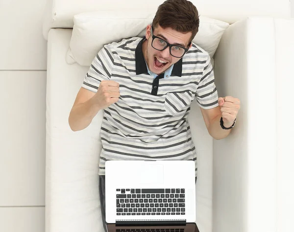 Feliz hombre moderno mira el portátil sentado en el sofá . — Foto de Stock