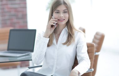 Ofiste oturan iş kadını cep telefonuyla konuşuyor.