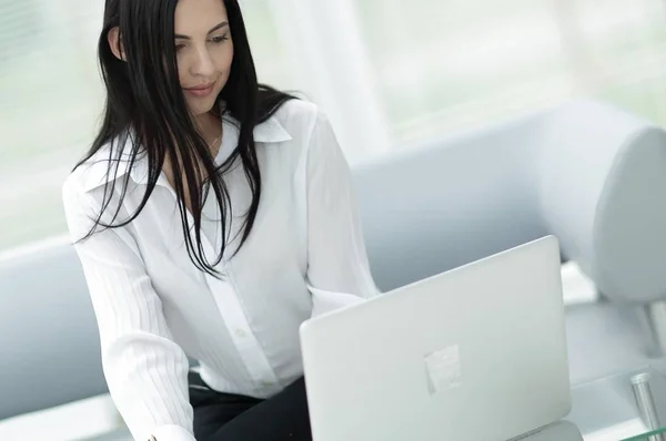 Framgångsrik ung kvinna sitter vid ett skrivbord på en suddig bakgrund. — Stockfoto