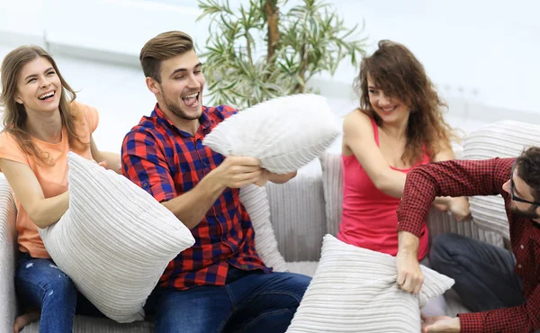 cheerful friends playing pillow fight, sitting on the couch