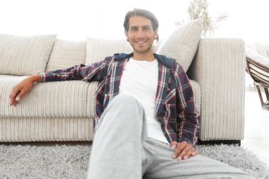 Kendine güvenen adam rahat bir oturma odasında halı üzerinde oturan.