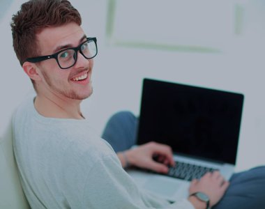 Genç adam evde dizüstü bilgisayar kullanıyor.