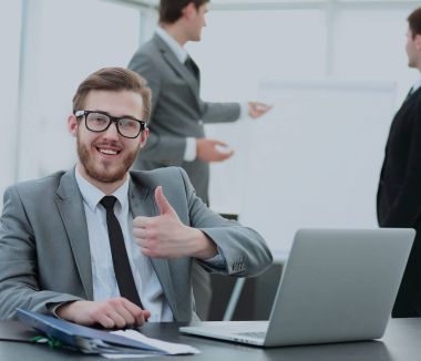 Yönetmen açık bir dizüstü bilgisayar ve kağıtları ile masada oturuyor.