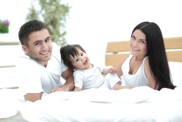 ベッドで横になっていると笑顔の赤ちゃんと幸せな若い家族 — ストック写真