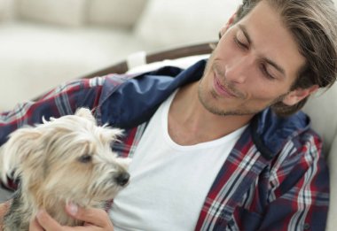 yakışıklı olan büyük bir koltukta otururken köpeğini okşayarak.