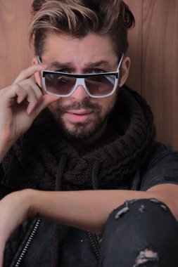 Ahşap bir arka planda yerde oturan kendinden emin bir adam.