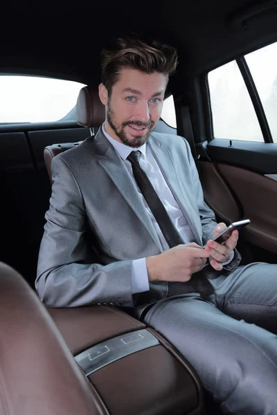 Homem de terno sentado no carro e ler mensagens no smartphone — Fotografia de Stock