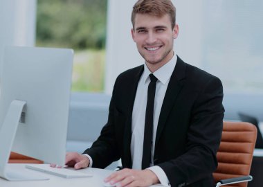 Modern bir ofiste bilgisayar üzerinde gülümseyen iş adamı