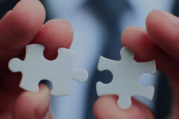 Geschäftsmann mit zwei weißen Puzzleteilen in der Hand, die die Lösung eines Problems, Wachstum und Entwicklung vorsehen. — Stockfoto
