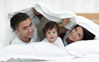 mutlu bir aile kameraya bakarken bir yorgan altında poz