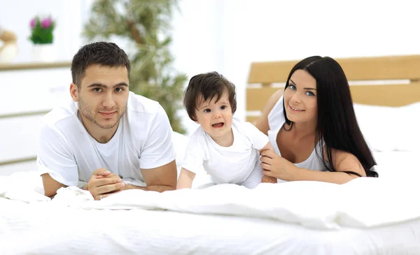 Portrait of happy young family lying in bed together — Stock Photo, Image