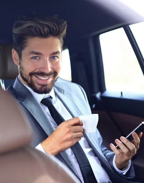 Uomo d'affari che beve caffè in auto con il telefono in mano — Foto Stock