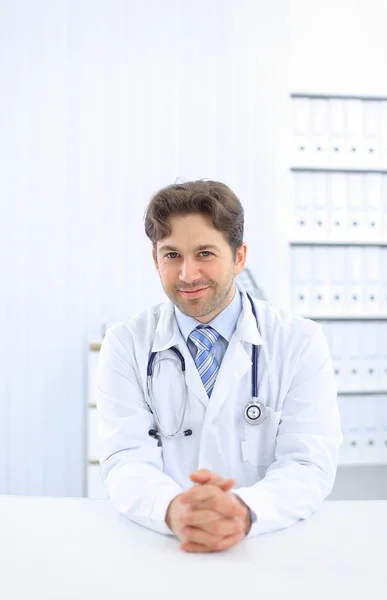 Bonito jovem médico de casaco branco está olhando para a câmera e sorrindo enquanto está no escritório — Fotografia de Stock