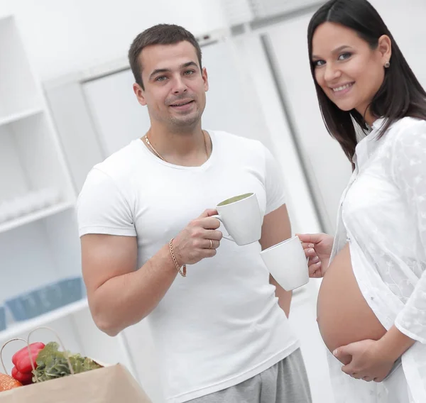 Marido e sua esposa grávida bebendo cacau, de pé na cozinha . — Fotografia de Stock