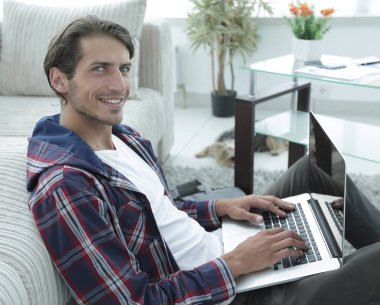 gülümseyen adam kanepede yakın katta oturan bir dizüstü bilgisayar ile