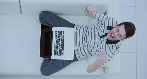 Ovanifrån av upphetsad ung man använder sin laptop i ljusa vardagsrum — Stockfoto