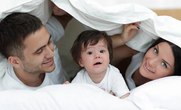 Familia feliz posando bajo un edredón mientras mira a la cámara — Foto de Stock