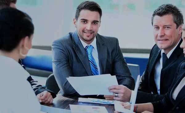 Улыбающийся молодой человек, сидящий на деловой встрече с коллегами — стоковое фото