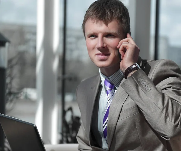 Attractive european guy talking on phone while using laptop. — Stock Photo, Image