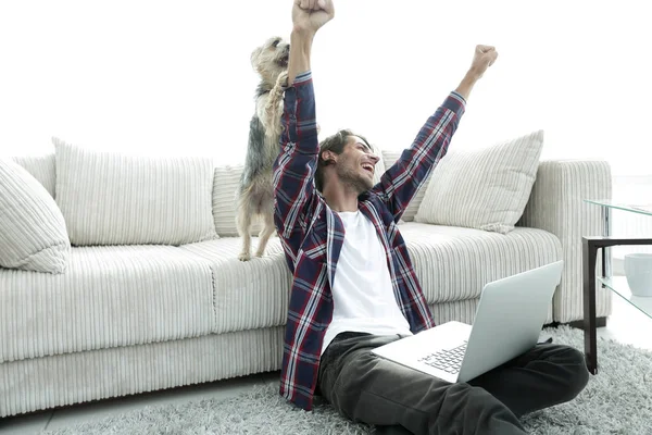Happy guy exults with his dog sitting near the sofa in the living room. — Stock Photo, Image