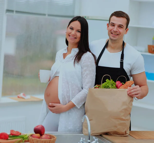 Беременная женщина с чашкой в руке, стоящая рядом с мужем на заднем плане кухни . — стоковое фото