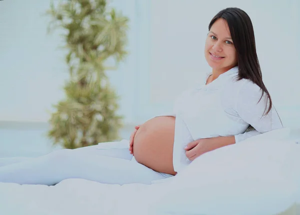 Mujer embarazada acostada en la cama, sonriendo y mirando a la cámara . — Foto de Stock