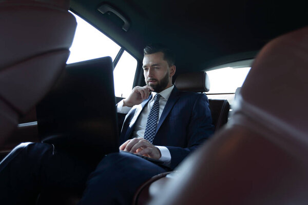 businessman working with laptop and looking out the window of a car